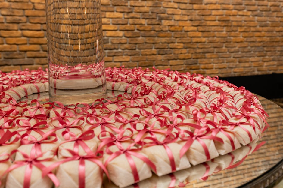 A beautifully arranged circle of small gifts tied with pink ribbons on a reflective surface.