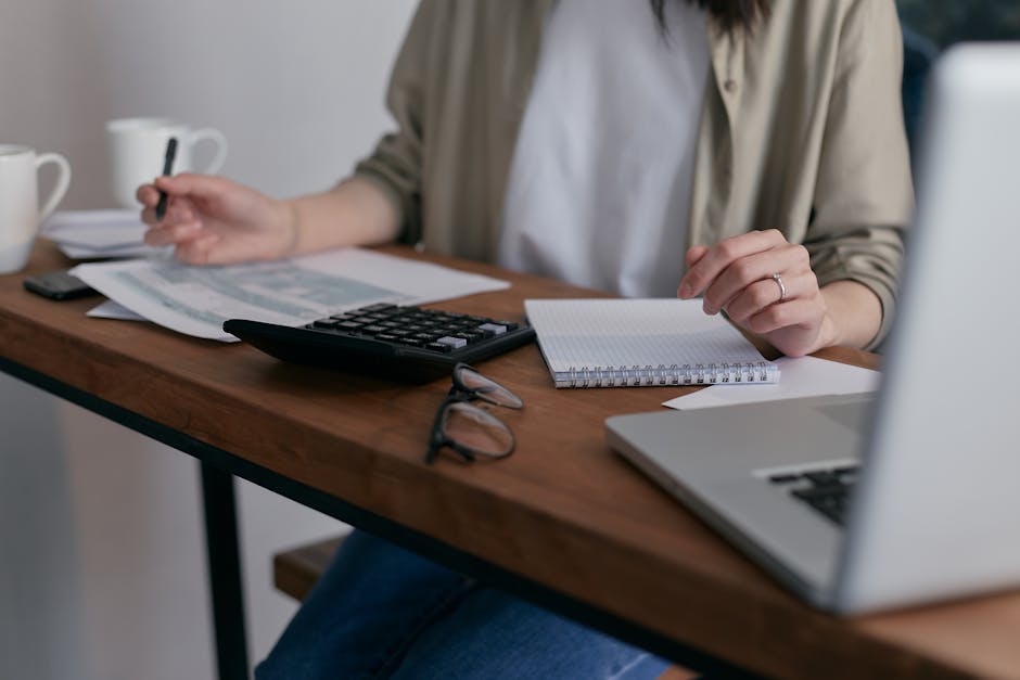 business credit cards - A woman manages finances at home, using a laptop and calculator on a wooden desk.
